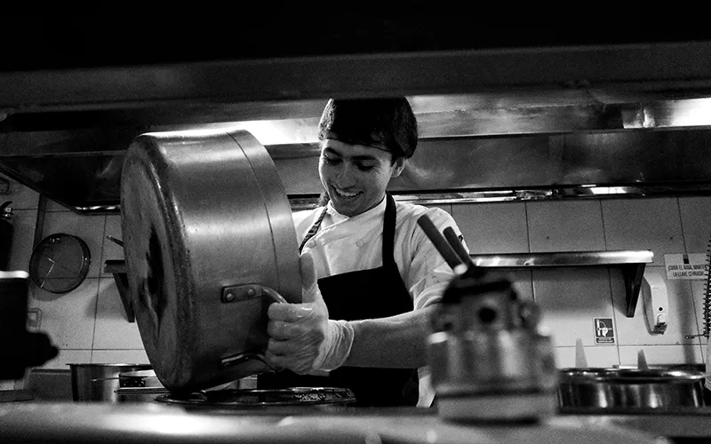 cocinero-sonrie-mientras-lava-olla-cocina Cocinero lava una olla de hacer sopas y sonrie mientras trabaja. Trabaja contento con sus compañeros