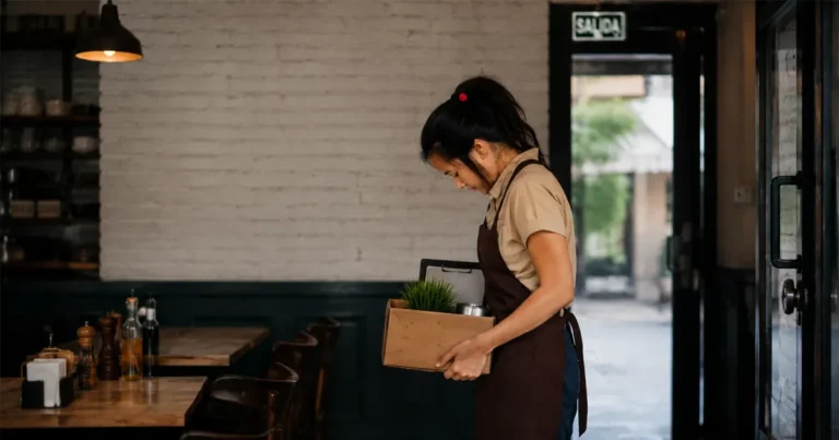 Empleada de restaurante saliendo del local cun una caja con sus pertenecias, despedida por falsas calumnias